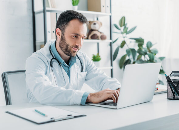 positive doctor sitting at workplace and using laptop